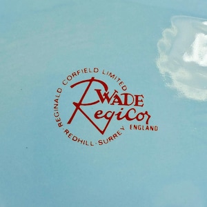May include: A light blue background with a red circular logo. The logo reads "Reginald Corfield Limited" around the perimeter, with "Wade Regicor" in the center and "Redhill Surrey England" at the bottom.