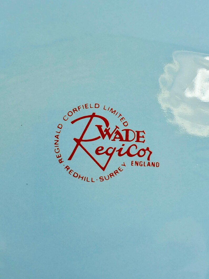 May include: A light blue background with a red circular logo. The logo reads "Reginald Corfield Limited" around the perimeter, with "Wade Regicor" in the center and "Redhill Surrey England" at the bottom.
