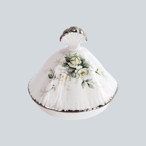 Può includere: Piatto coperto in porcellana bianca con bordo e manico argentati. Il coperchio è decorato con un motivo floreale di rose gialle e bianche con foglie verdi. Il piatto è contrassegnato con il numero "#1" in nero.