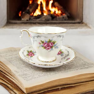 Peut inclure: Une tasse à thé et une soucoupe blanches avec un motif floral de roses roses et de fleurs bleues. La tasse à thé et la soucoupe sont posées sur une pile de vieux livres.