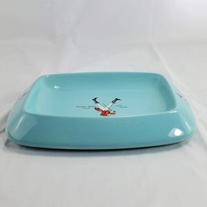 May include: A rectangular, light blue ceramic ashtray. The ashtray has rounded corners and a slightly raised edge. The center of the ashtray features a graphic of a skier. Text on the ashtray reads "Colorado Rockies" and "Ski Team".