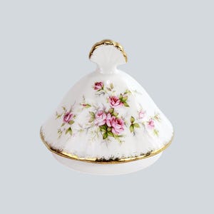 Può includere: Un coperchio in porcellana bianca con un delicato motivo floreale di rose rosa e foglie verdi. Il coperchio a cupola presenta un bordo smerlato con finiture dorate e una maniglia decorativa con accenti dorati sulla parte superiore, etichettato con il numero 1.