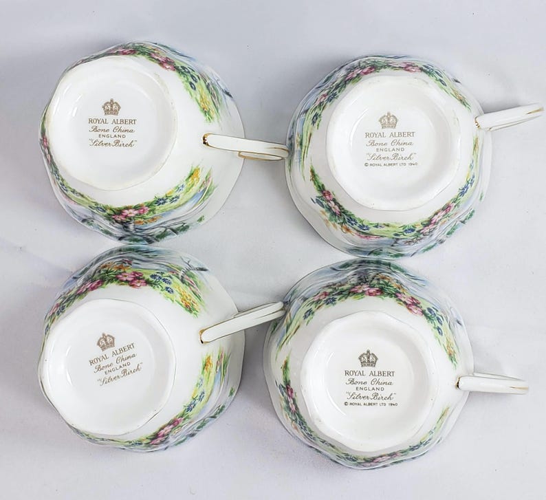 Puede incluir: Cuatro tazas de t&eacute; de porcelana fina Royal Albert Silver Birch. Cada taza presenta un dise&ntilde;o de paisaje con flores rosas y moradas, follaje verde y un cielo azul claro. Las tazas tienen ribetes y asas doradas.