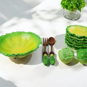 May include: A set of green and yellow ceramic salad bowls with a lettuce design. The set includes a large salad bowl, four smaller bowls, and a wooden salad fork and spoon.