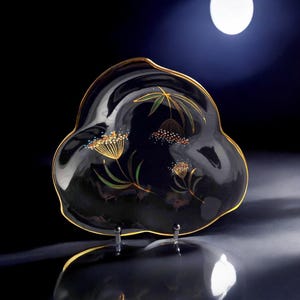 May include: A black glass serving dish with a gold rim and a floral design in gold and green. The dish is on a stand with three legs.