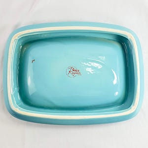 May include: A rectangular, turquoise ceramic dish with a white rim. The interior is a solid turquoise color. The dish has rounded corners and a slightly raised edge. The bottom of the dish has a red and white logo that reads "Wade Regicor".