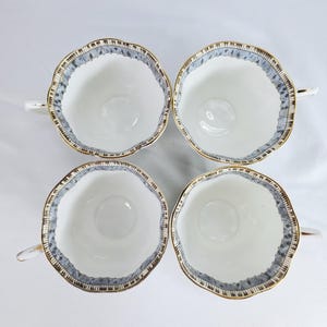 Puede incluir: Cuatro tazas de t&eacute; blancas con borde festoneado y ribete dorado. El borde presenta un patr&oacute;n azul y marr&oacute;n. Cada taza tiene un asa peque&ntilde;a. Las tazas est&aacute;n dispuestas en forma cuadrada.