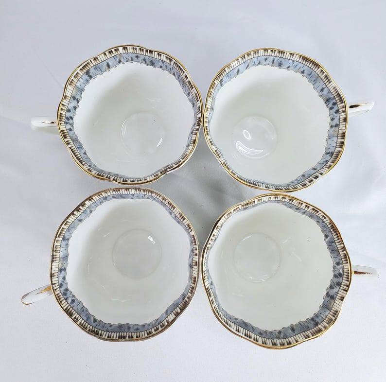 Puede incluir: Cuatro tazas de t&eacute; blancas con borde festoneado y ribete dorado. El borde presenta un patr&oacute;n azul y marr&oacute;n. Cada taza tiene un asa peque&ntilde;a. Las tazas est&aacute;n dispuestas en forma cuadrada.