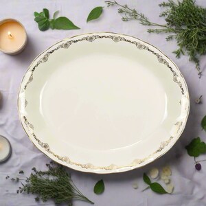 May include: A white oval serving platter with a gold decorative border. The platter is on a white tablecloth with green and white sprigs of greenery.