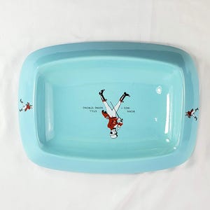 May include: A rectangular, light blue ceramic tray with rounded corners. The tray features a central illustration of a soldier and the text "BORN 1820 - STILL GOING STRONG". Additional soldier illustrations are on the tray's edges.