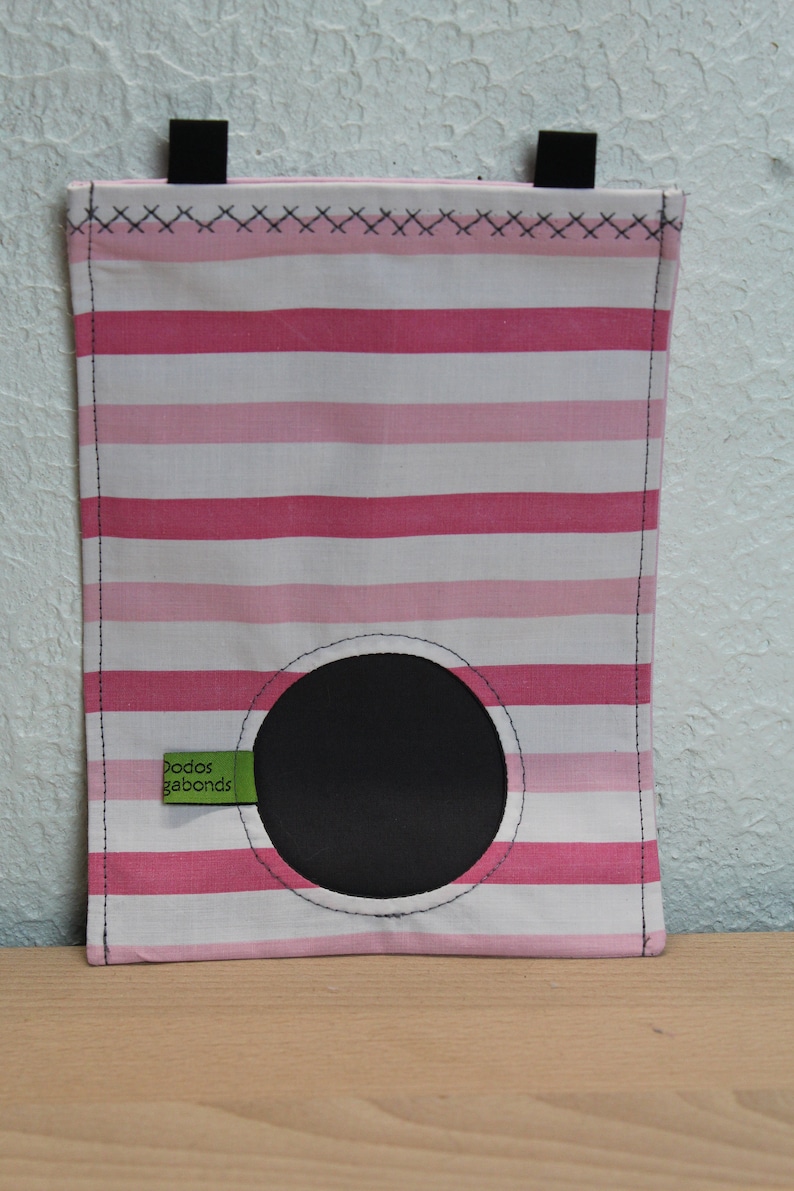 May include: Pink and white striped fabric bag with a black circle cutout and a green label that says "Dodos Gabonds".