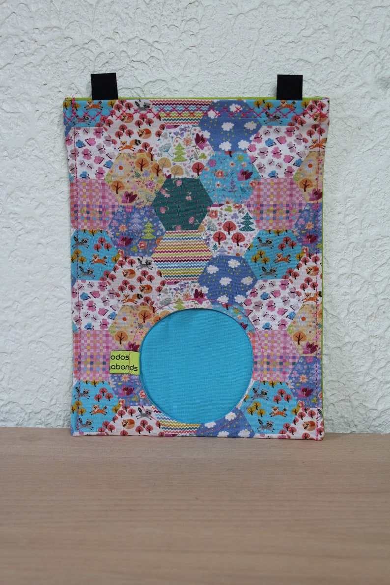 May include: A colorful fabric pouch with a hexagonal patchwork design featuring a variety of floral and woodland patterns. The pouch has a circular opening and a turquoise lining. The text "odos labonds" is printed on the front of the pouch.