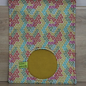 May include: A white fabric bag with a colorful geometric pattern and a round opening. The bag has a green label that says "Dodos gabonds".