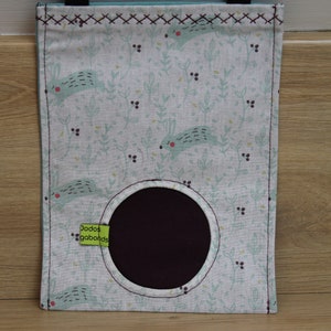 May include: A white fabric storage bag with a green and blue bunny pattern. The bag has a round opening and a green label that says "Dodos gababonds".