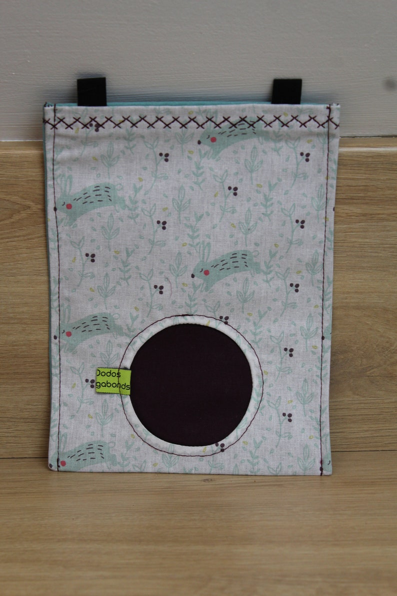 May include: A white fabric storage bag with a green and blue bunny pattern. The bag has a round opening and a green label that says "Dodos gababonds".