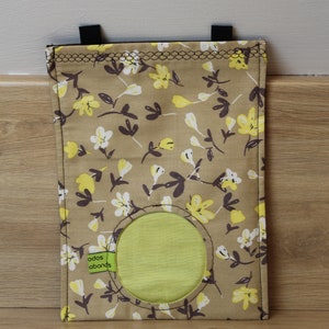 May include: A brown fabric bag with a yellow and white floral pattern. The bag has a round opening with a green fabric lining. The bag has two black straps at the top and a green label that says "odos abounds".