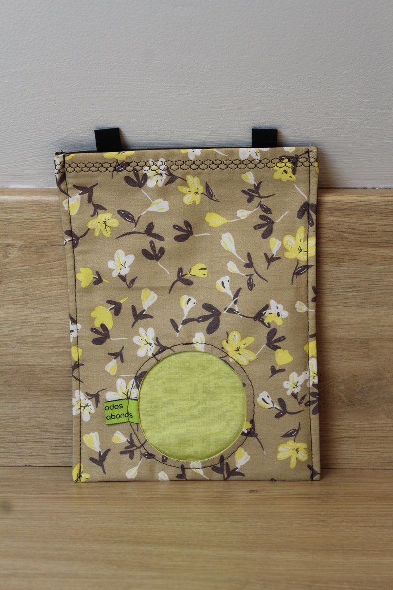 May include: A brown fabric bag with a yellow and white floral pattern. The bag has a round opening with a green fabric lining. The bag has two black straps at the top and a green label that says "odos abounds".