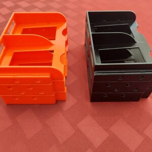 May include: Two 3D printed storage organizers, one orange and one black, with multiple compartments. The organizers are stacked on top of each other.