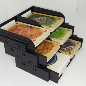 May include: Black plastic card holder with five compartments for organizing cards. The holder is stacked in a tiered design. Each compartment has a different colored card with a design on it.