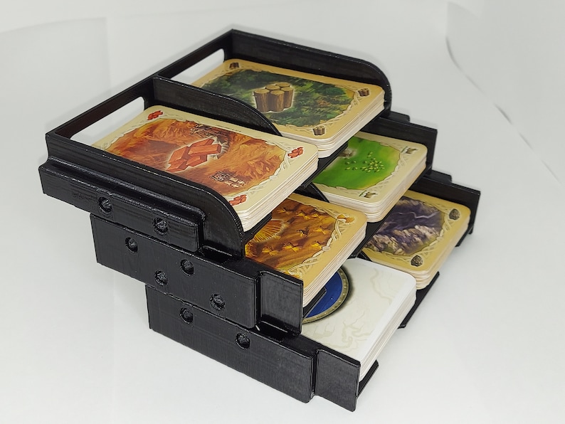 May include: Black plastic card holder with five compartments for organizing cards. The holder is stacked in a tiered design. Each compartment has a different colored card with a design on it.