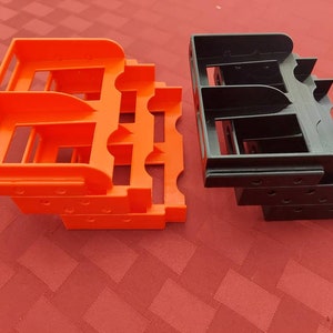 May include: Two stacks of 3D printed storage organizers. One stack is orange and the other is black.