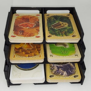 May include: A black plastic organizer with four compartments for storing game cards. Each compartment has a different image of a card from the game.