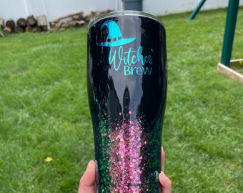 May include: Black tumbler with a green and pink glitter design. The tumbler has a witch's hat graphic and the text "Witches' Brew".