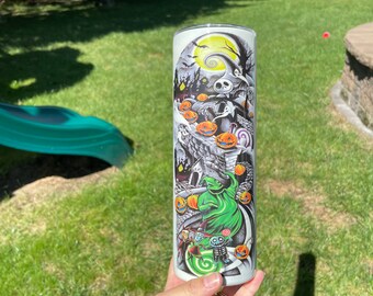May include: A cylindrical tumbler featuring a detailed graphic print inspired by The Nightmare Before Christmas, showcasing Jack Skellington, Oogie Boogie, and various characters amidst a dark, spooky landscape with bright orange pumpkins.