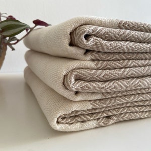 Könnte beinhalten: Ein Stapel aus vier gewebten Handtüchern in Beige und Braun. Die Handtücher sind gefaltet und auf einer weißen Oberfläche gestapelt.