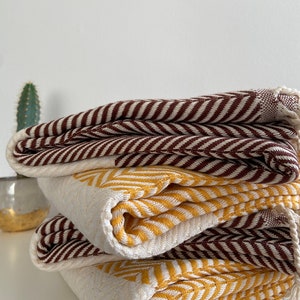 May include: A stack of three woven cotton blankets with a chevron pattern. The top blanket is brown and white, the middle blanket is yellow and white, and the bottom blanket is brown and white.