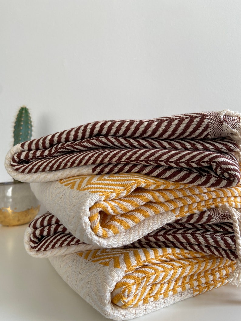 May include: A stack of three woven cotton blankets with a chevron pattern. The top blanket is brown and white, the middle blanket is yellow and white, and the bottom blanket is brown and white.