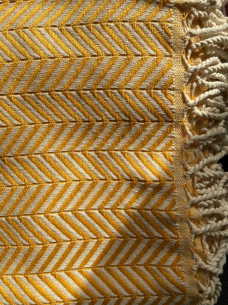 May include: A yellow and white throw blanket with a chevron pattern and fringe on the edges.