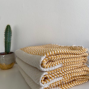 May include: A stack of three yellow and white striped towels folded neatly on a white surface. The towels have a chevron pattern.