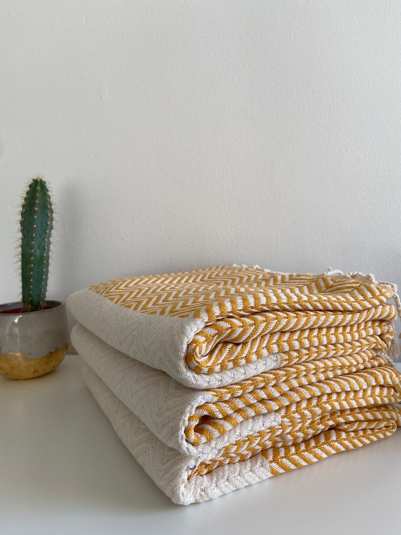 May include: A stack of three yellow and white striped towels folded neatly on a white surface. The towels have a chevron pattern.