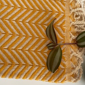 May include: A yellow and white woven throw blanket with a fringe border. The blanket has a chevron pattern and is made of a soft, textured fabric.