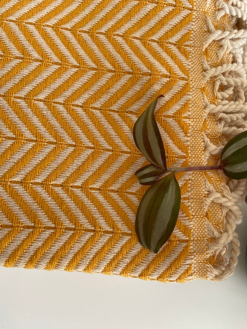 May include: A yellow and white woven throw blanket with a fringe border. The blanket has a chevron pattern and is made of a soft, textured fabric.