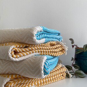 May include: A stack of four folded towels in a chevron pattern. The top towel is blue and white, the second is yellow and white, the third is white and blue, and the bottom towel is yellow and white.