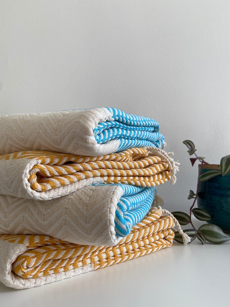 May include: A stack of four folded towels in a chevron pattern. The top towel is blue and white, the second is yellow and white, the third is white and blue, and the bottom towel is yellow and white.
