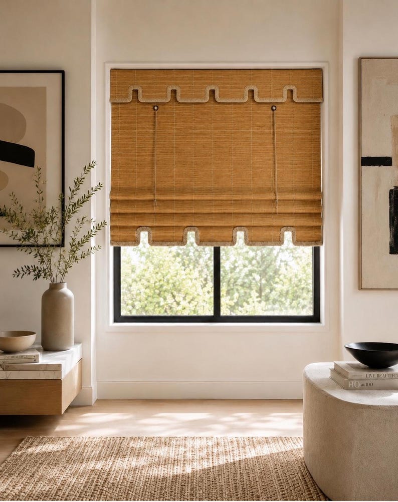 May include: A woven bamboo roman shade in a natural tan color featuring a scalloped edge design along the top valance and the bottom hem. The shade includes thin vertical pull cords and a textured, grid-like pattern across the material.
