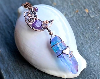 Op de afbeelding: Een hanger met koperdraad gewikkeld met een blauwe en paarse kristallen punt met een klein hartje. De hanger hangt aan een koperen ketting met een paarse en heldere kristallen accent.