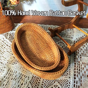 May include: Two oval-shaped woven rattan baskets, one nested inside the other. The baskets are made of natural brown rattan and have a hand-woven design. 100% Hand Woven Rattan Basket.