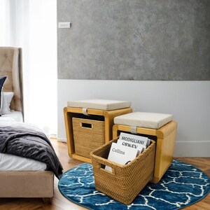 May include: Two wooden storage ottomans with cushioned tops. The ottoman on the right has a woven basket pulled out, revealing magazines inside. The ottomans are on a blue and white patterned rug.
