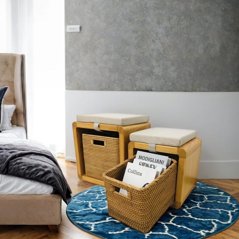 May include: Two wooden storage ottomans with cushioned tops. The ottoman on the right has a woven basket pulled out, revealing magazines inside. The ottomans are on a blue and white patterned rug.