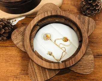 May include: A wooden star-shaped jewelry box with a white velvet interior. The box has a ring holder and a small compartment for a necklace or earrings. The box is made of dark walnut wood and has a natural finish.
