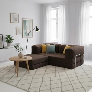 Puede incluir: Un sal&oacute;n moderno con un sof&aacute; seccional marr&oacute;n con cojines amarillos y azules. Una mesa de centro redonda de madera descansa sobre una alfombra estampada. Una l&aacute;mpara de pie negra y obras de arte enmarcadas completan el espacio.