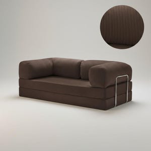 Puede incluir: Un sof&aacute; de pana marr&oacute;n con reposabrazos redondeados y una base rectangular. El sof&aacute; tiene un dise&ntilde;o moderno con un marco de metal en el lateral. La imagen incluye un primer plano de la tela de pana.