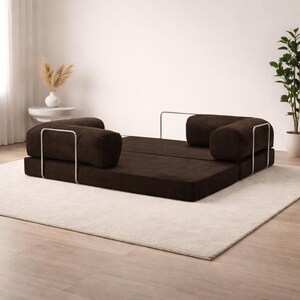 Puede incluir: Sof&aacute; convertible de pana marr&oacute;n con dos cojines cil&iacute;ndricos y base rectangular. El sof&aacute; tiene estructura met&aacute;lica y est&aacute; sobre una alfombra clara. Dise&ntilde;o moderno y minimalista.