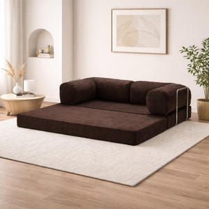 Puede incluir: Un sof&aacute; convertible de pana marr&oacute;n con un perfil bajo. El sof&aacute; tiene un dise&ntilde;o modular con una base plana y respaldos acolchados. El marco est&aacute; acentuado con metal plateado. El sof&aacute; est&aacute; sobre una alfombra blanca en una habitaci&oacute;n bien iluminada.