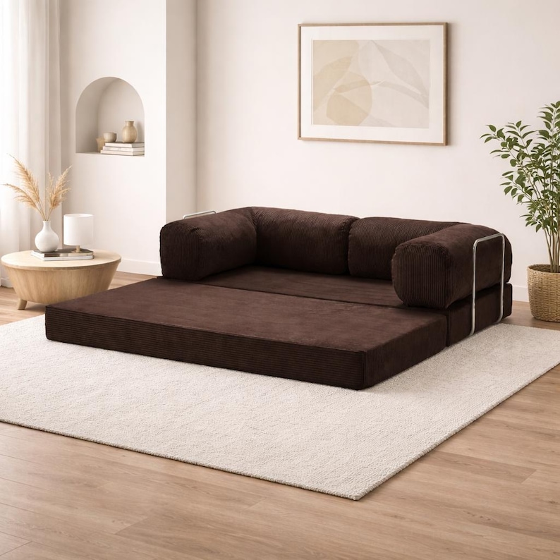 Puede incluir: Un sof&aacute; convertible de pana marr&oacute;n con un perfil bajo. El sof&aacute; tiene un dise&ntilde;o modular con una base plana y respaldos acolchados. El marco est&aacute; acentuado con metal plateado. El sof&aacute; est&aacute; sobre una alfombra blanca en una habitaci&oacute;n bien iluminada.