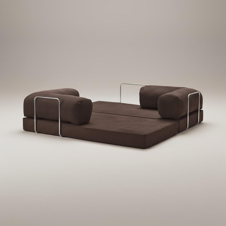 Puede incluir: Un sof&aacute; cama convertible marr&oacute;n moderno con dos respaldos cil&iacute;ndricos y un asiento plano. El sof&aacute; cuenta con una estructura met&aacute;lica y est&aacute; dise&ntilde;ado para un uso vers&aacute;til. El dise&ntilde;o general es minimalista y contempor&aacute;neo.